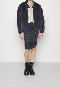 Donkergrijze bomberjack met een zachte faux bont textuur, gecombineerd met een strakke marineblauwe rok met ruches. Zwarte veterboots met een chunky zool.