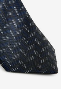 Navy blue tie featuring a chevron pattern with textured fabric and contrasting silver dots, creating a structured design with sharp angles.