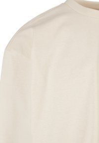 Lys beige bomulls T-skjorte med en glatt tekstur, rund hals, og korte ermer. Har et minimalistisk design uten mønstre eller detaljer.