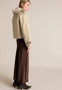 Beige kort jacka med grå huva, kombinerad med en lång brun kjol och mörka klackade ankelstövlar. Slät tyg, enkel design.