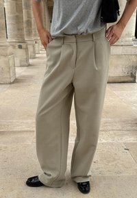 Jasnobeżowe spodnie z zakładkami wykonane z gładkiego materiału, z wysokim stanem i szerokimi nogawkami, w połączeniu z błyszczącymi czarnymi butami.