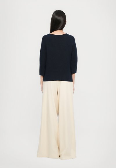 Dunkelblaues, strukturiertes Strickpullover mit Dreiviertelärmeln, kombiniert mit cremefarbenen weiten Hosen. Einfaches, klares Design ohne sichtbare Muster.
