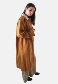 Lange mosterdkleurige jas met een witte kraag, met een los ontwerp en zijzakken. De stof lijkt glad met een lichte glans.