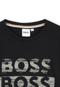 Crna majica s okruglim izrezom, s istaknutim iznošenim bijelim natpisom "BOSS" na prednjoj strani. Mekani materijal s opuštenim krojem.