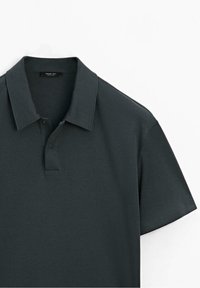 Polo vert foncé à manches courtes avec col et deux boutons noirs visibles près de l'encolure.