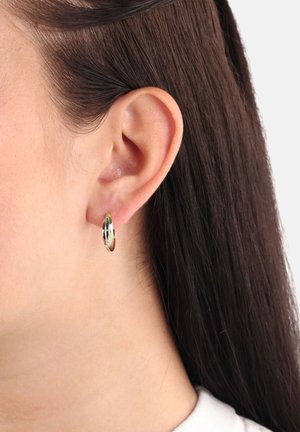 Pendiente de aro de oro y plata exhibido en la oreja de un modelo. El diseño presenta una superficie suave y pulida con diferentes grosores.