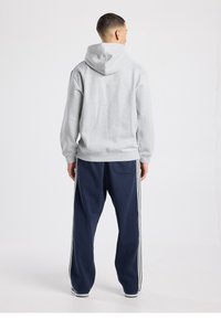 Sweat à capuche gris avec cordon de serrage, assorti à un pantalon de survêtement bleu marine avec des bandes blanches sur les côtés et une poche arrière supplémentaire.