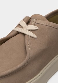 Κοντινή λήψη μπεζ καστόρινου καθημερινού παπουτσιού με στρογγυλεμένη μύτη, μπεζ κορδόνια δεμένα σε απλό κόμπο και ανοιχτόχρωμη ραφή στη σόλα.