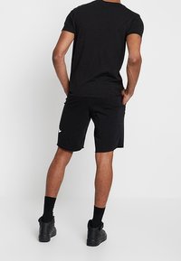 Musta t-paita ja shortsit, valmistettu pehmeästä kankaasta. Paidassa on pyöreä pääntie, ja shortseissa on logo sivussa. Mustat lenkkarit.