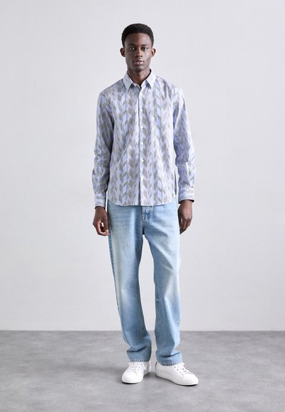 Camisa abotonada con un patrón geométrico en azul y blanco, combinada con jeans de color azul claro y zapatillas blancas. Tejido suave, corte ajustado.