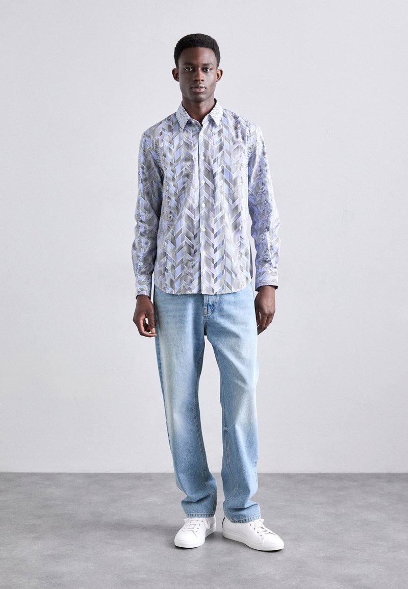 Skjorte med knapper i et geometrisk blått og hvitt mønster, parret med lyseblå jeans og hvite sneakers. Glatt stoff, skreddersydd passform.