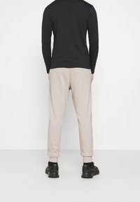 Black long-sleeve shirt and light beige jogger pants, featuring elastic cuffs and a relaxed fit, paired with black athletic shoes.