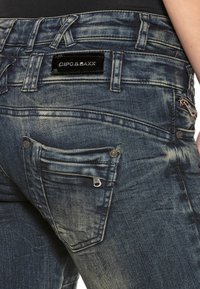 Denim-Jeans mit einem blassen blauen Finish, fünf Taschen einschließlich einer mit Reißverschluss, und einem schwarzen Logo-Patch am Bund.