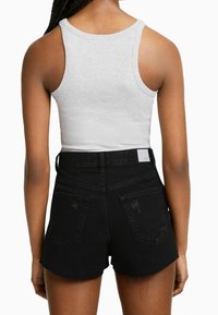 Pantalones cortos de mezclilla negra con cintura alta, dobladillo deshilachado y dos bolsillos traseros. La modelo lleva una camiseta sin mangas de canalé gris claro.