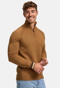 Tan gebreide pullover met een halve ritssluiting en geribde manchetten. Bevat textuurstof en gestreepte accenten in marineblauw en crème bij de polsen.