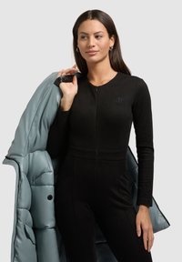 Mono negro ajustado con manga larga y escote redondo. Lleva una chaqueta acolchada de color azul claro sobre el brazo, con textura acolchada.