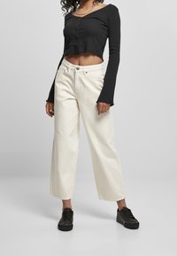 Svart croppad långärmad skjorta med knappar, matchad med vita vida jeans och svarta sneakers; har råa fållar och en avslappnad passform.