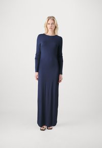 Navy blue long-sleeve maxi dress in a fitted design, with a crew neck and smooth texture. Paired with black flip-flops.