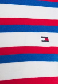 Nærbillede af rød, hvid og blå horisontalt stribet stof med et lille rektangulært broderet logo i rød, hvid og sort.