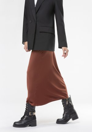 Blazer doppiopetto nero, gonna midi in raso color ruggine e stivali combat neri con lacci e dettaglio decorativo in fibbia.