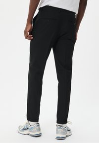 Svarta byxor med smal passform, som har två bakfickor och en mjuk yta. Bärs med ljusgrå och blå löparskor.