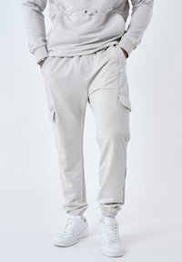 Lichtgrijze joggingbroek gemaakt van zachte stof, met ritssluitingen in de zakken en elastische boorden, gecombineerd met witte sneakers.