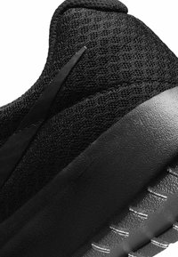 Närbild av hälen på en svart idrottssko som visar den strukturerade mesh-överdelen, den släta mellansulan och mönstret på sulan.