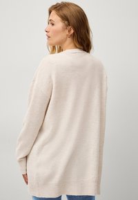 Maglione oversize beige chiaro in morbido materiale a maglia. Presenta un collo rotondo e polsini a coste, con un orlo posteriore leggermente più lungo.