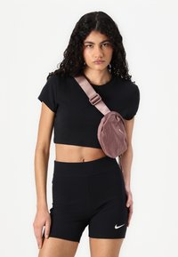 T-shirt noir court et shorts noirs taille haute. Sac à épaule en tissu violet avec fermeture éclair et logo Nike à l'avant. Cheveux bouclés visibles.