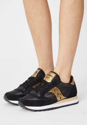 Scarpe da atletica nere e oro con un design in camoscio e mesh, caratterizzate da una finitura testurizzata e un intersuola bianca. Logo iconico sulla linguetta.