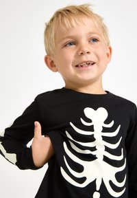 Schwarzes Langarm-T-Shirt mit einem weißen Skelettdruck auf der Vorderseite und den Ärmeln. Weiches Baumwollmaterial; runder Halsausschnitt.