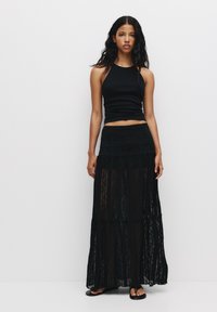 Jupe maxi en dentelle noire avec un design à volants, présentant une taille texturée et un tissu transparent, associée à un débardeur noir ajusté.