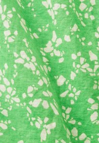 Tissu vert avec des motifs floraux et de pétales blancs irréguliers créant un motif dispersé sur la surface texturée du tissu.