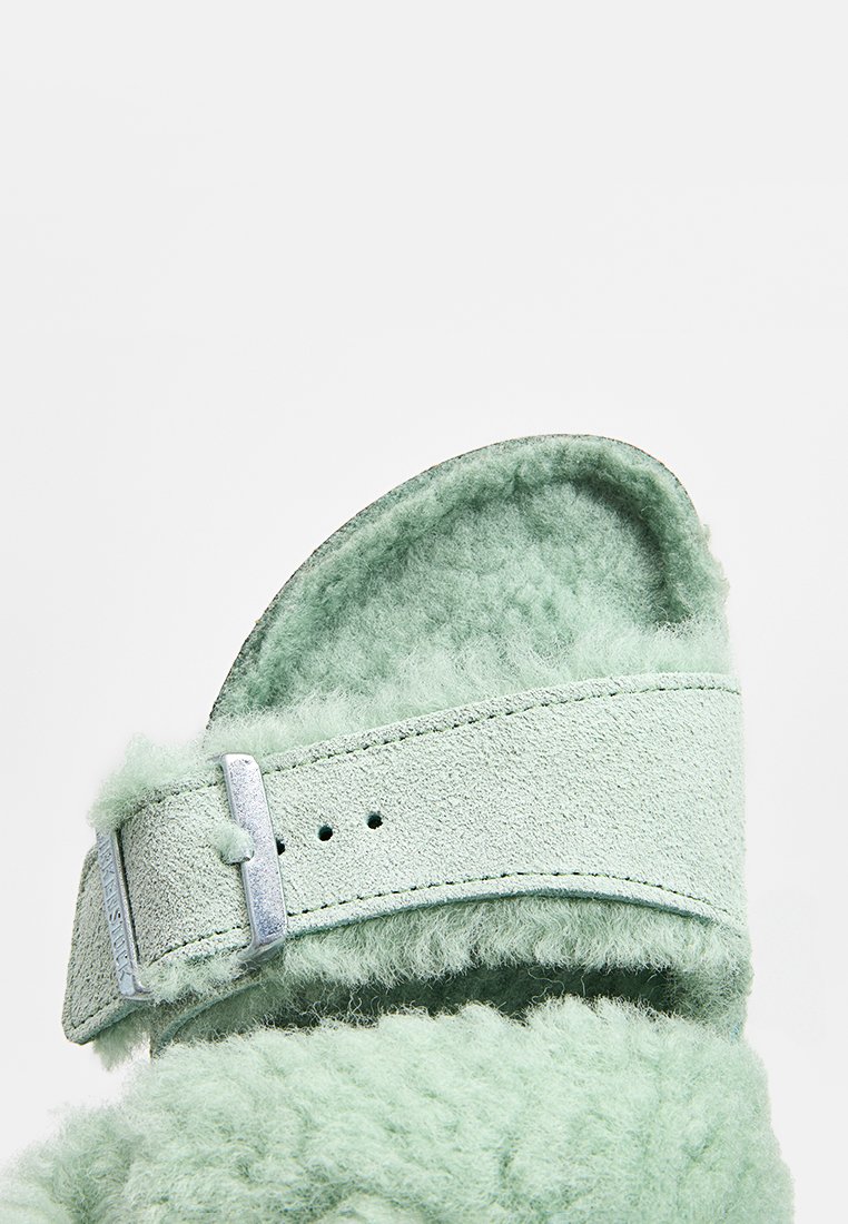 Mintgrüne Rutschsandale mit kuscheliger Textur, aus Wildledermaterial und einem metallischen Schnallen-Riemen. Vorformbare Fußbett für zusätzlichen Komfort.