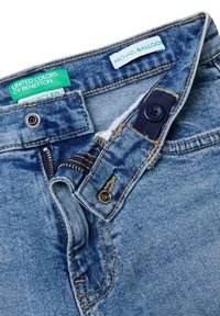 Modré džíny z denimu s částečně otevřeným zipem a knoflíkem, zobrazující zelené štítky "United Colors of Benetton" a bílé štítky "Michael-Balloon".