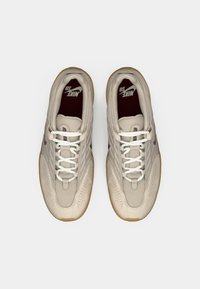 Μπεζ αθλητικά παπούτσια με υφασμάτινη επάνω επιφάνεια με υφή, δερμάτινες λεπτομέρειες, λευκά κορδόνια και σόλες από καουτσούκ καραμέλας, με μπορντό εσωτερική σόλα.