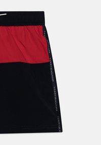 Pantaloni da bagno neri con un pannello rosso nella parte superiore. Presenta una cintura elastica con coulisse e dettagli del logo laterali in bianco.