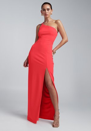 Czerwona, wieczorowa sukienka na jedno ramię z wysokim rozcięciem na udzie. Gładka, dopasowana faktura. Metaliczne akcenty na ramieniu i minimalistyczne detale projektu.