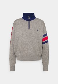 Sudadera gris con un cuello azul marino, cierre de media cremallera y rayas rojas y azules en las mangas. Presenta un pequeño logo en el pecho.