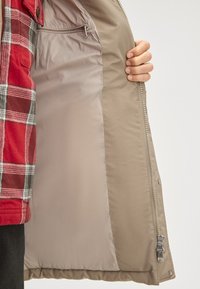 Beżowa kurtka z gładką nylonową podszewką, z kieszenią na zamek błyskawiczny oraz dwukierunkowym zamkiem. Zewnętrzna warstwa ma delikatny połysk.