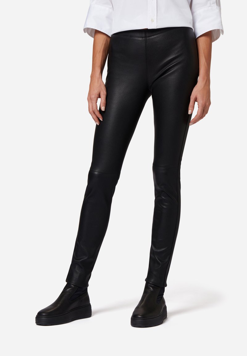 Zwarte nep leren leggings met een slim fit, voorzien van een hoge tailleband en een gladde, glanzende textuur. Gecombineerd met zwarte instap schoenen.