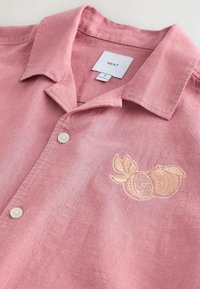 Rosa Leinenhemd mit kurzem Kragen, zwei weißen Knöpfen und beiger Obststickerei auf der linken Brust, Marke Next, Größe M.