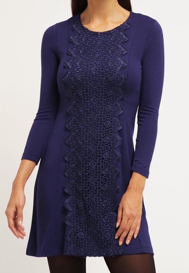 Marinblå klänning med långa ärmar och ett texturerat spetspanel i mitten. Spetsen har cirkulära mönster och vågiga kanter.