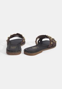 Bruine leren sandalen met twee brede banden, voorzien van gouden studs, een zachte zwarte voetbed en een bruine rubberen zool.