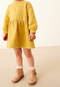 Vestido de forro amarillo con motivos de arcoíris, mangas abullonadas y cintura fruncida. Botines beige con ribete de encaje rosa y detalle de cremallera.
