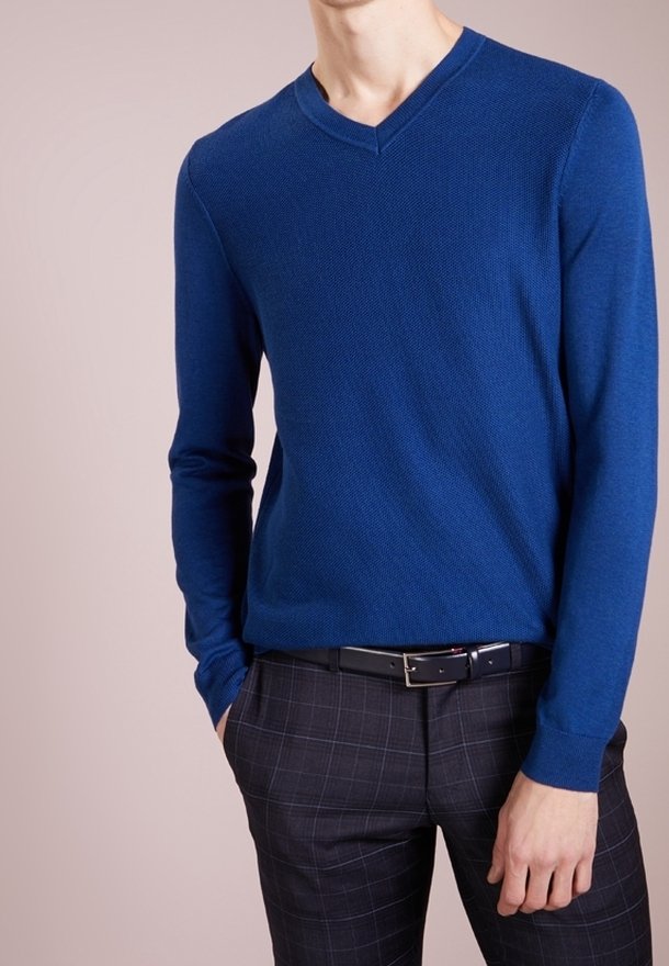 Modrý svetr s výstřihem do V a texturovanou tkaninou, doplněný tmavě kostkovanými kalhotami a černým páskem. Dlouhé rukávy, přiléhavý střih, hladký povrch.