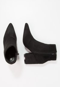 Botines negros de ante, con punta afilada, cremallera lateral y un tacón grueso con un acabado brillante.