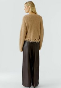 Beige, flauschiger Pullover mit fransigem Saum, kombiniert mit dunkelbraunen, weit geschnittenen Lederhosen. Die gesamte Textur wirkt weich und plüschig.
