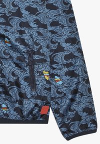 Marineblauem Stoff mit blauen Wellenmustern, bunten Surfbrett-Motiven, einer schwarzen Reißverschlusstasche und einem roten Markenpatch nahe dem Bündchen.