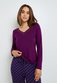 Haut violet à manches longues avec un col en V et des finitions en dentelle. Associé à un bas de pyjama à motifs comportant de petits designs floraux dans des tons de violet.